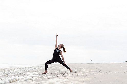 Eine Frau steht in Yogaposition am Strand von Spiekeroog 
