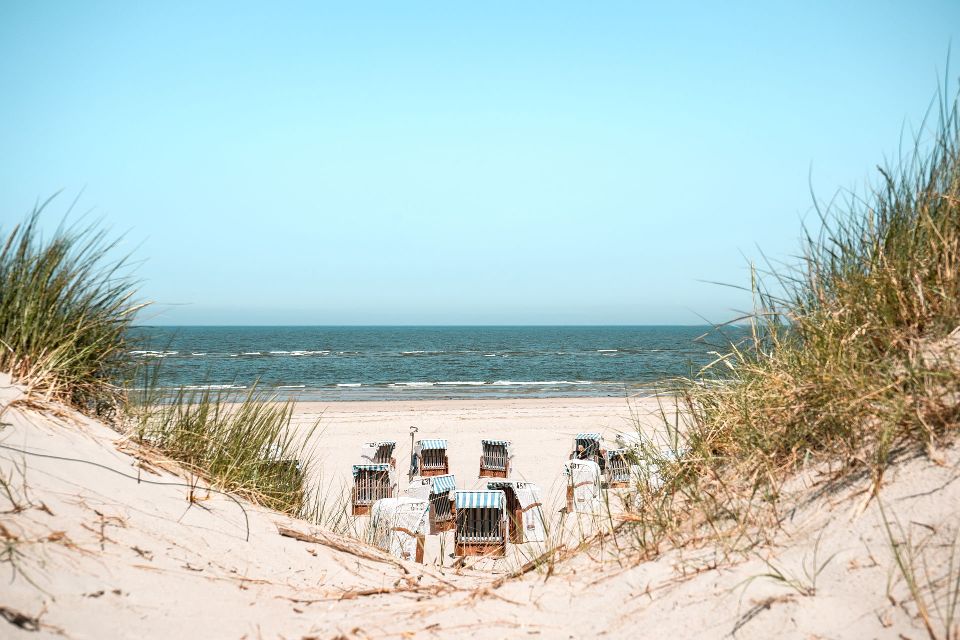 Blick durch ein Dünental auf Strandkörbe am Strand von Spiekeroog.