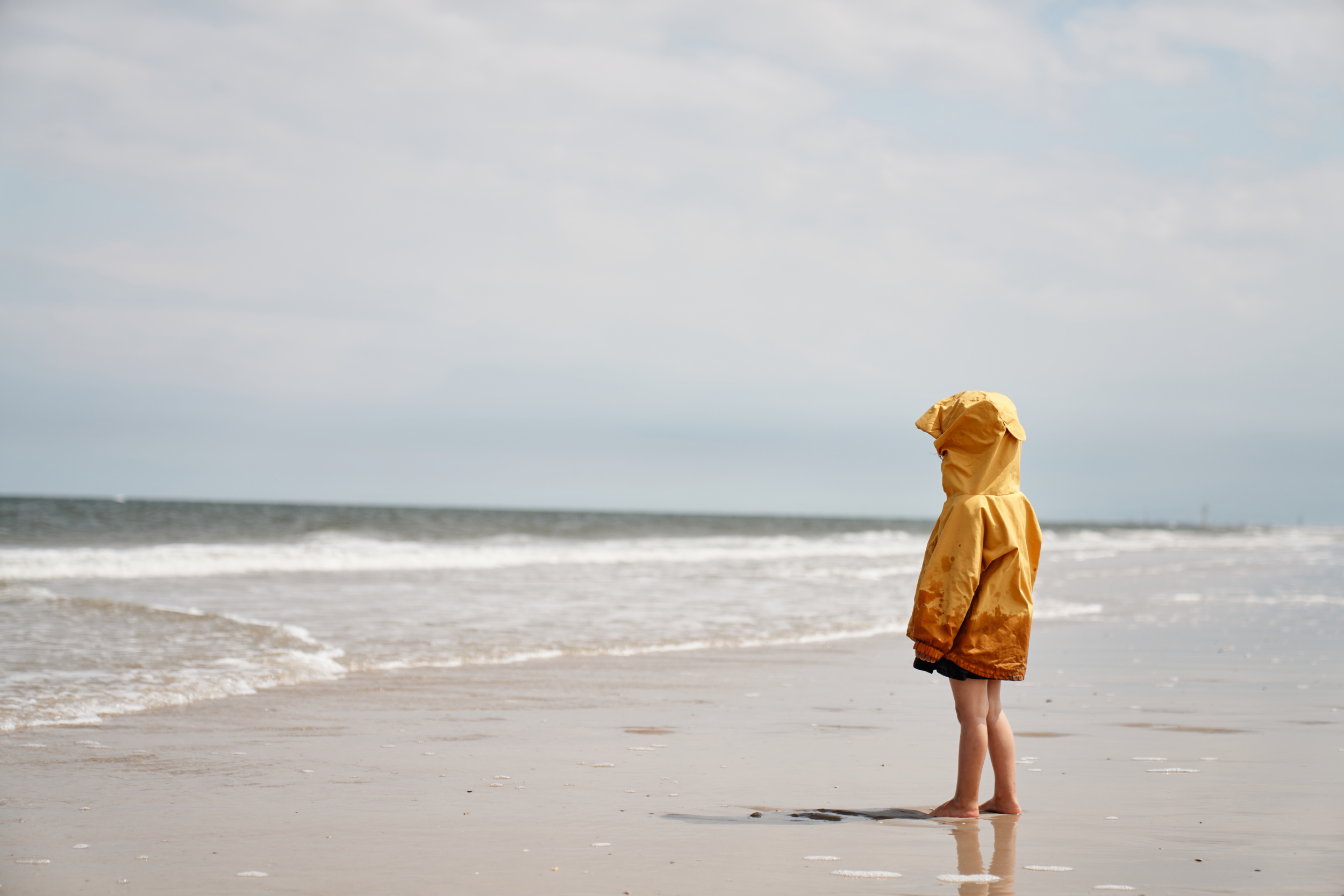 Ein Kind steht mit Regenjacke am Spiekerooger Strand