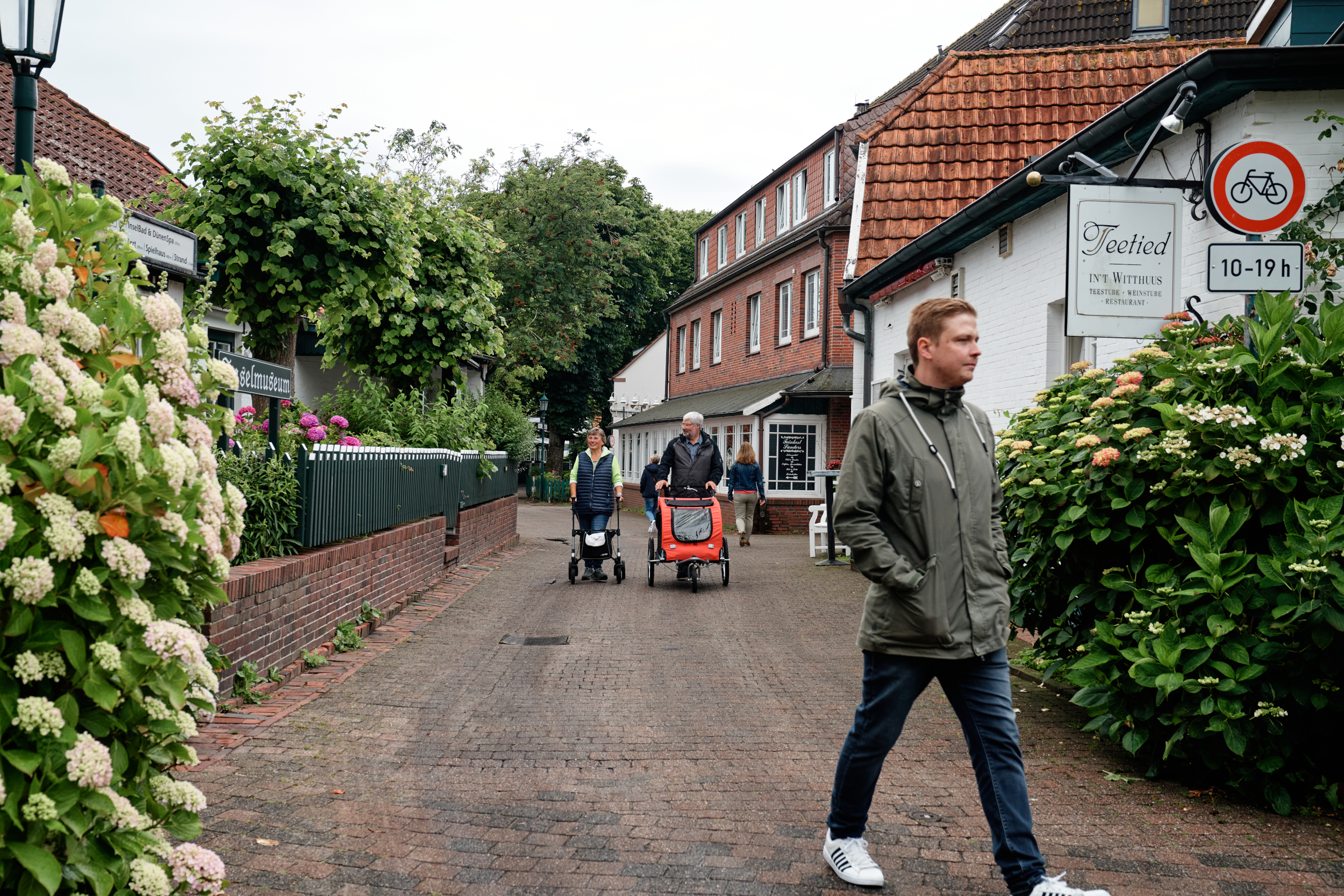 Ein Mann mit Croozer und eine Frau mit Rollator auf einem Spaziergang durch das Spiekerooger Dorf