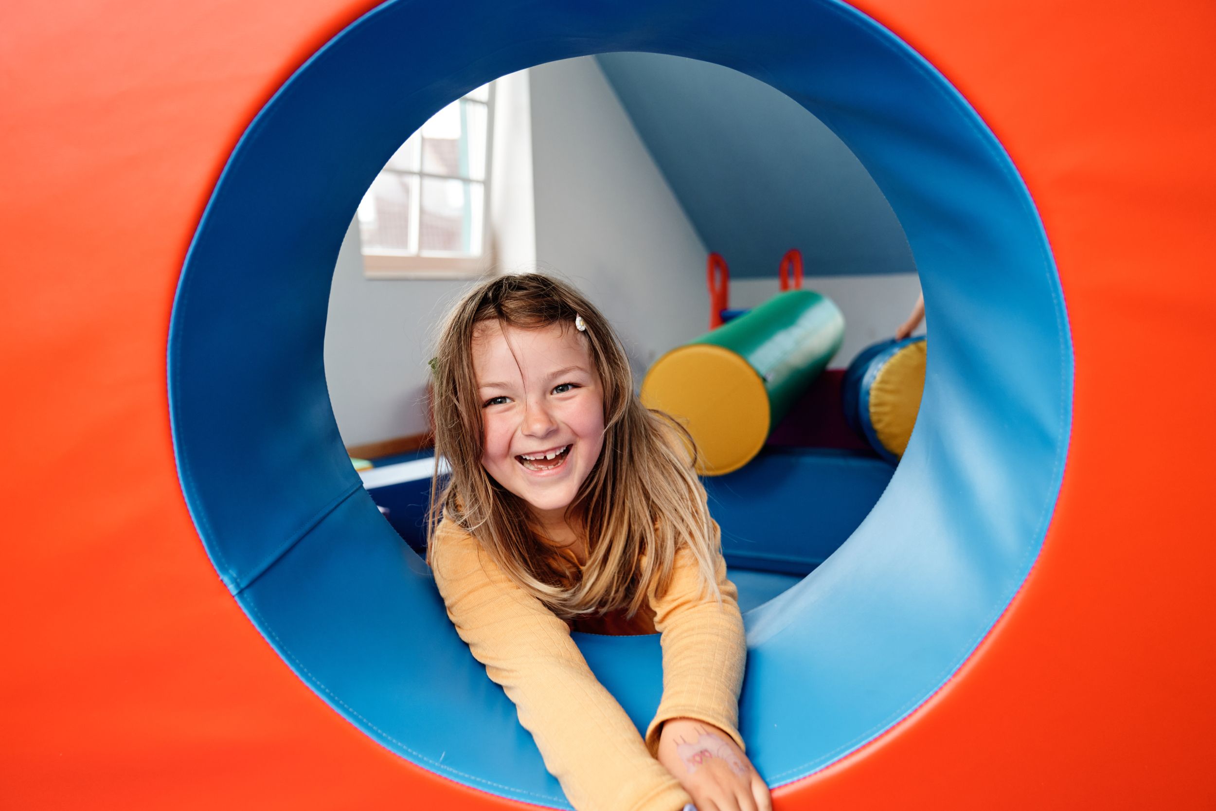 Ein Mädchen schaut aus einem Spielzeug-Tunnel.