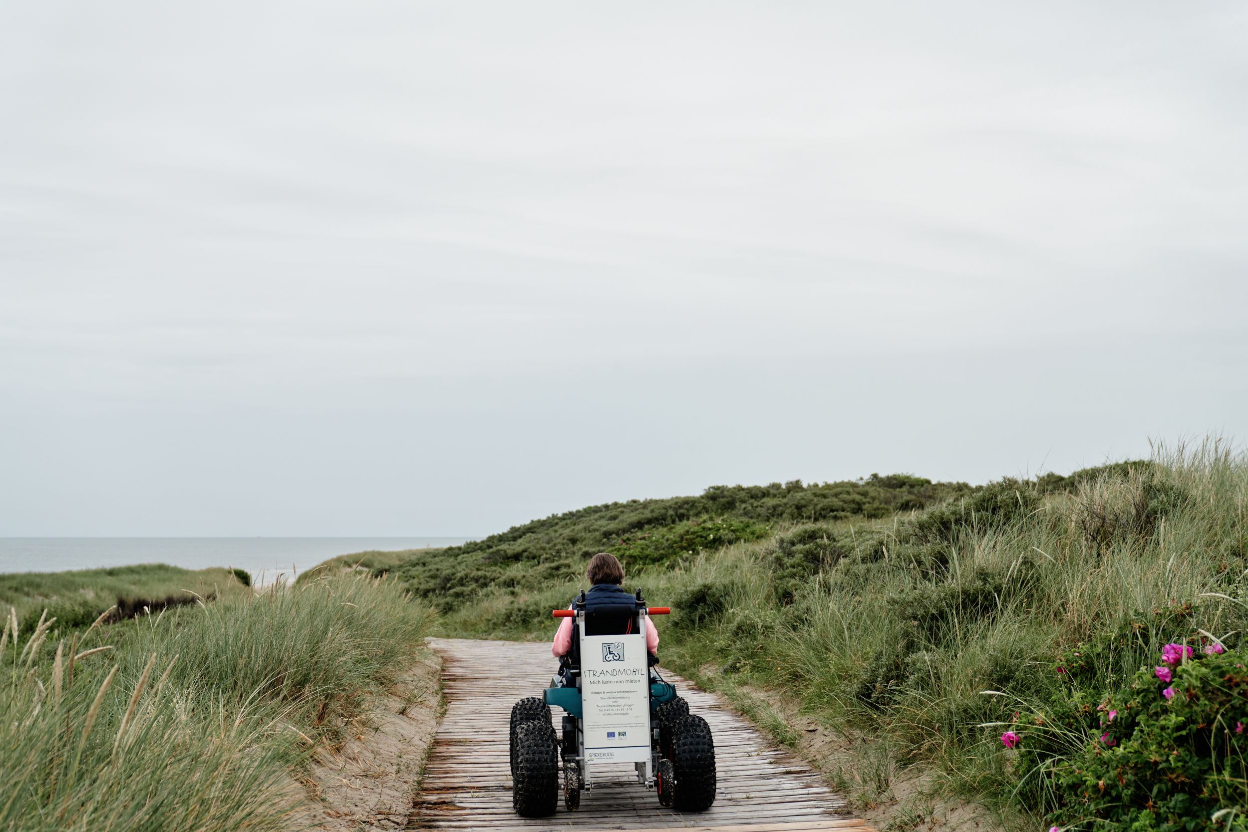 Eine Frau mit Strandrollstuhl auf dem Weg zum Spiekerooger Strand